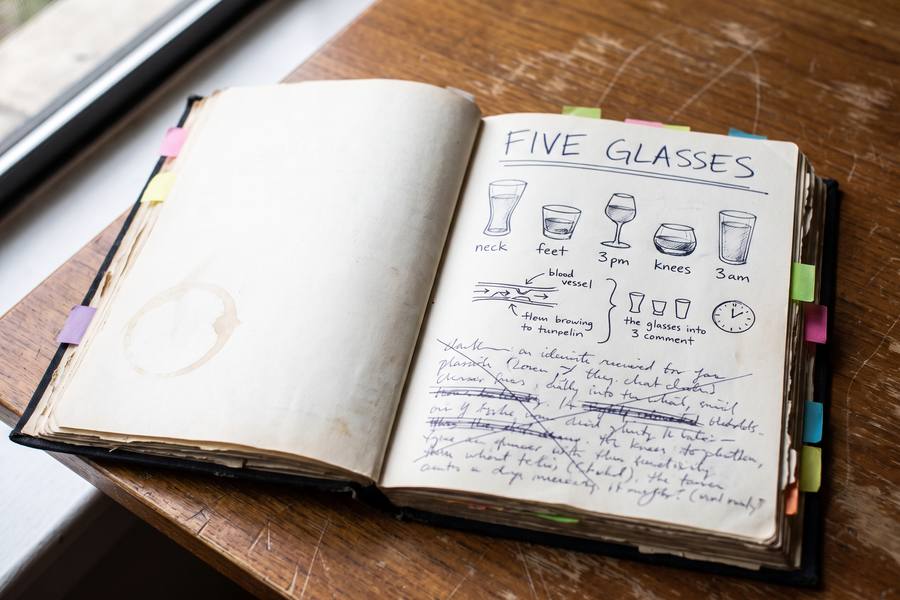 The notebook open on a page headed five glasses: five drawn glasses labelled neck, feet, 3 pm, knees and 3 am, a sketch of a blood vessel, a clock